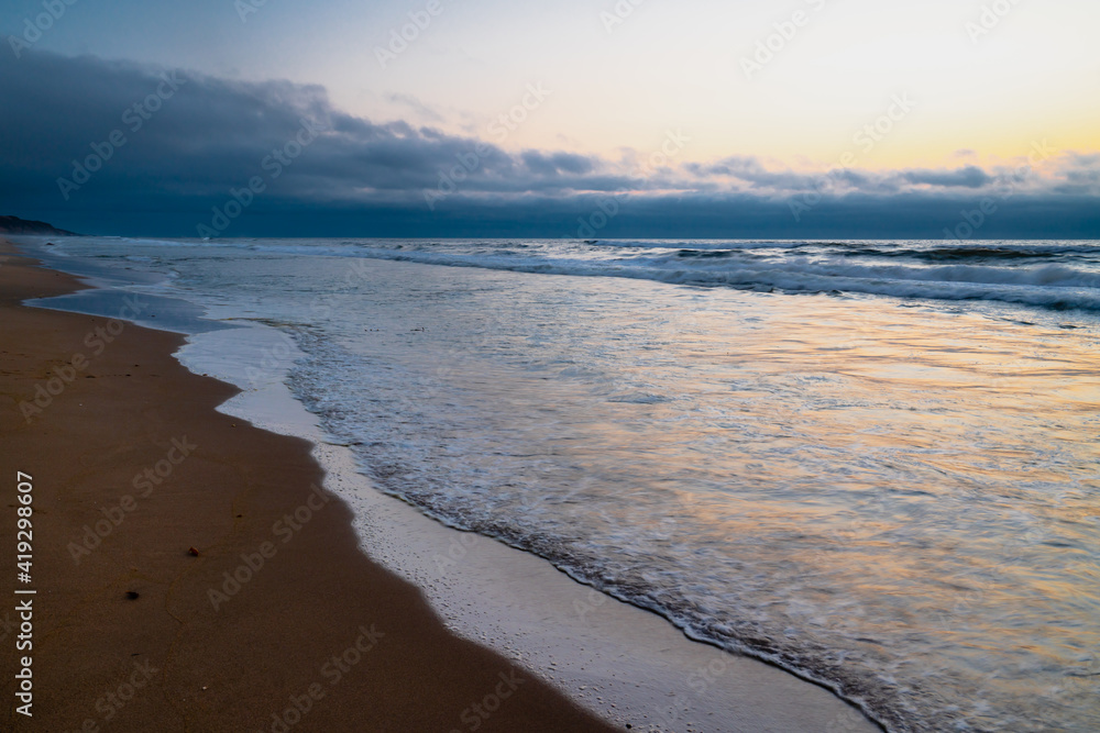 Sunset on the beach, abstract background. Sandy beach, blue sea with golden reflections, and cloudy sky background