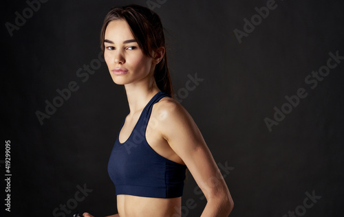 sportswoman with dumbbells in her hands on a black background slim figure short top