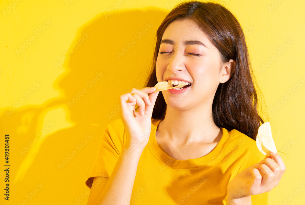 Young Asian girl eating snack on yellow background Young Asian girl eating snack on yellow background