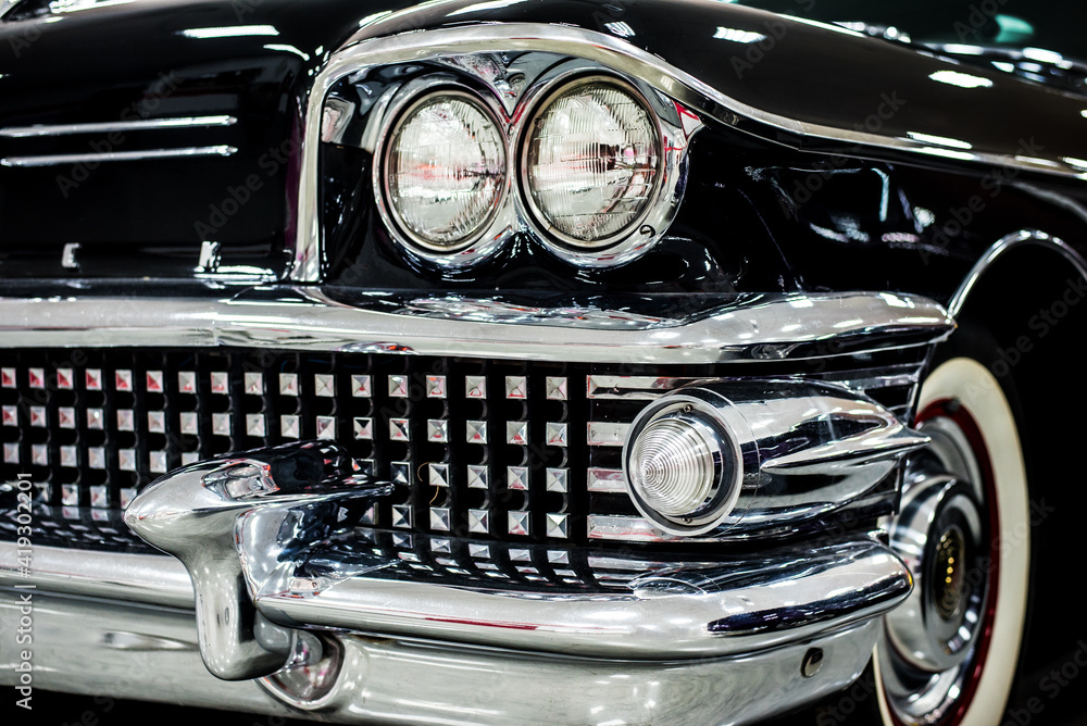 chrome radiator grille with retro car headlight close-up with blurred background