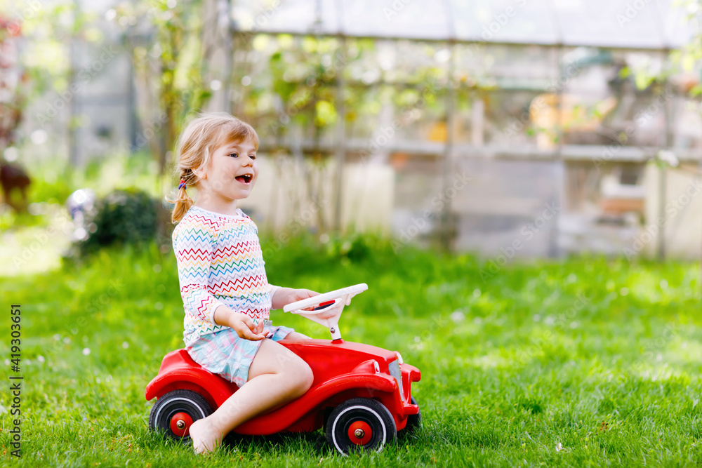 Little active adorable toddler girl driving toy car and having fun with playing, outdoors. Gorgeous happy healthy child enjoying warm summer day. Smiling stunning kid in gaden Little active adorable toddler girl driving toy car and having fun with playing, outdoors. Gorgeous happy healthy child enjoying warm summer day. Smiling stunning kid in gaden