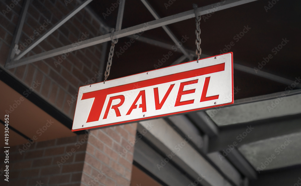 Metal travel sign hanging of a building outside. White store sign with debossed red Metal travel sign hanging of a building outside. White store sign with debossed red