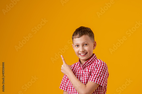 cheerful, happy child points up, copying the place for the text. A smiling, enthusiastic teenage boy in a plaid shirt shows off. Advertising concept.