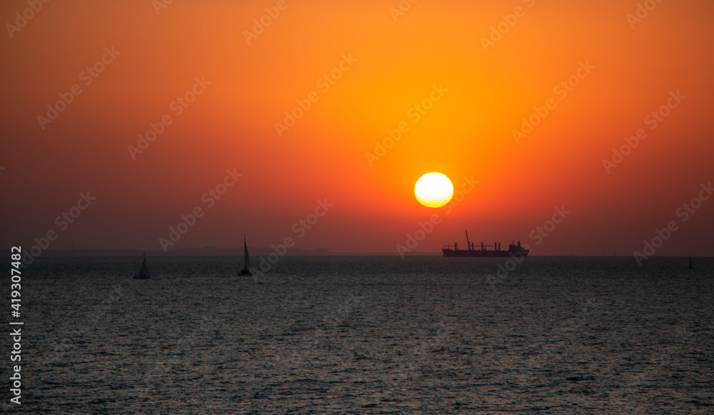 Red sunrise sky at sea and silhouettes of ships sailing on the sea.