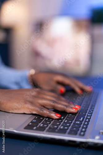 Side view of african woman hands typing on laptop working on deadline for company. Employee using modern technology network wireless doing overtime.