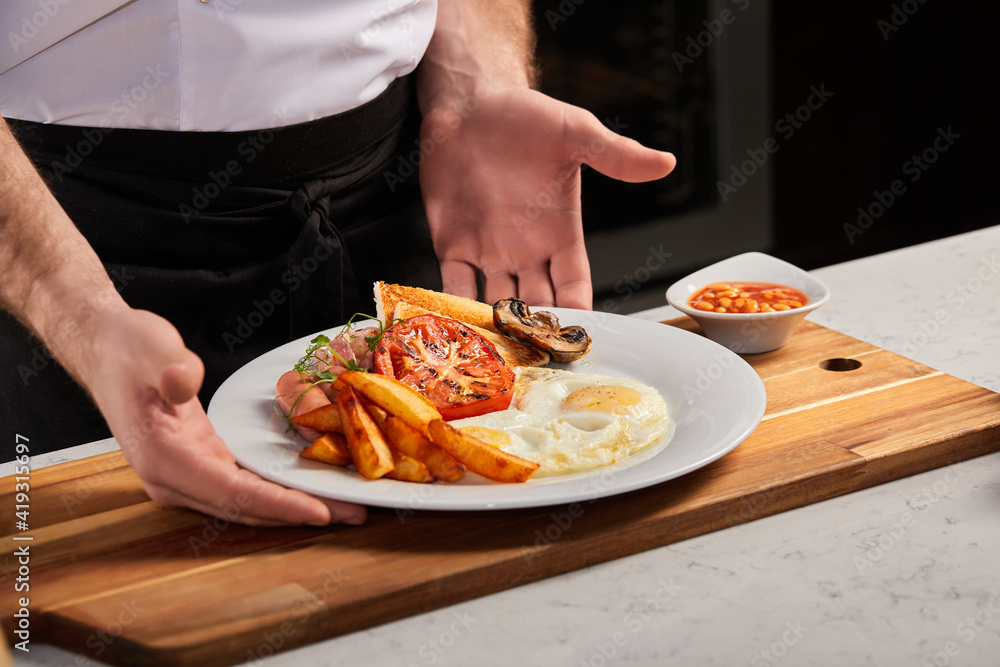 Breakfast on white plate in restaurant, copy space. fried eggs, roasted bacon, fries and vegetables prepared by professional chef cook. european cuisine concept. man putting plate on wooden board