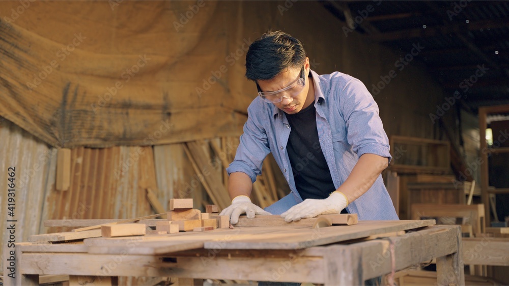 Carpenter working on wood craft at workshop to produce construction material or wooden furniture. The young Asian carpenter use professional tools for crafting. DIY maker and carpentry work concept. Carpenter working on wood craft at workshop to produce construction material or wooden furniture. The young Asian carpenter use professional tools for crafting. DIY maker and carpentry work concept.
