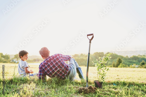 Foto Grandfather and grandson sitting in the meadow at sunset