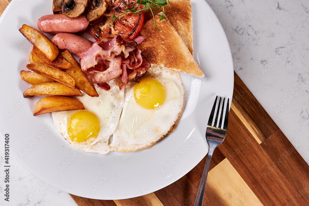 cooked American Breakfast on white plate in restaurant, copy space. fried eggs, roasted bacon, fries and vegetables prepared by professional chef cook. european cuisine concept cooked American Breakfast on white plate in restaurant, copy space. fried eggs, roasted bacon, fries and vegetables prepared by professional chef cook. european cuisine concept