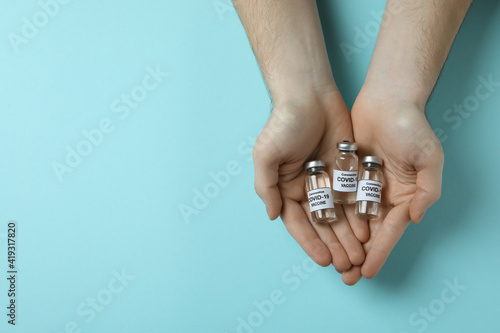 Male hands hold vials of Covid - 19 vaccine on blue background