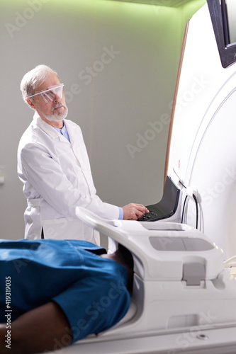 Male Patient Lying On MRI Machine While Elderly professional Doctor Operating It  Radiologist in White Medical Suit Treating Patient  Examining Health