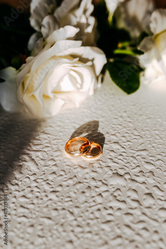 Obraz na płótnie Golden wedding rings under sun. White roses on white table. Fresh flowers on white background. Wedding rings with water drops and flowers. w salonie