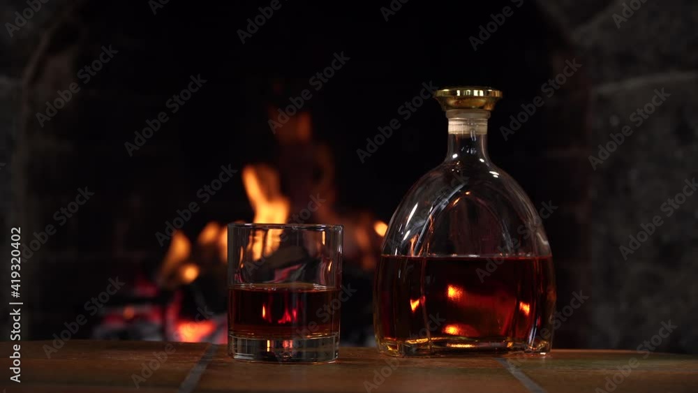 Bottle and glass with whiskey or cognac. Burning Fire In The Fireplace. Warmth and home comfort. 4K Bottle and glass with whiskey or cognac. Burning Fire In The Fireplace. Warmth and home comfort. 4K