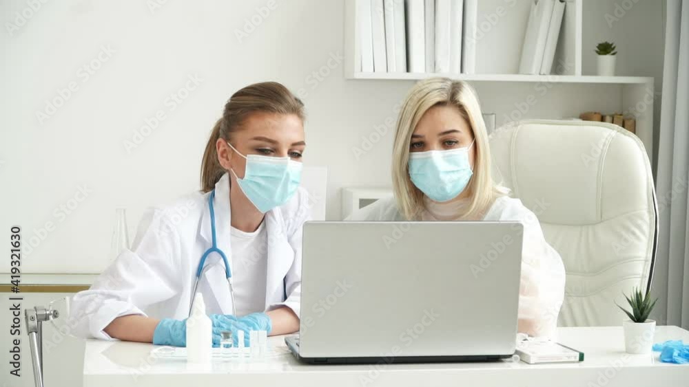 Team of female doctors in medical white coats and protective masks work and discuss patients diagnosis at laptop in clinic. Coronavirus, covid-19 concept Team of female doctors in medical white coats and protective masks work and discuss patients diagnosis at laptop in clinic. Coronavirus, covid-19 concept