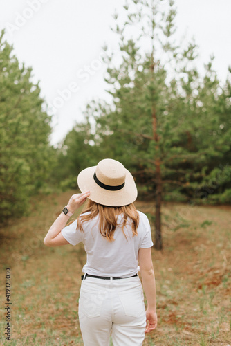 a girl in a straw hat and white clothes walks through the woods © Natalia