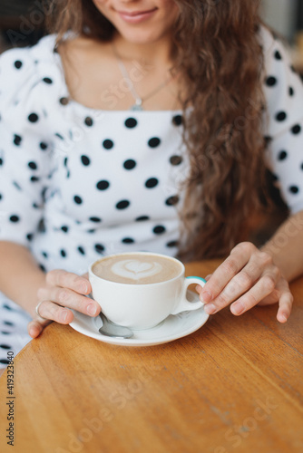 girl in a white dress with polka dots drinks coffee at a table in a cafe