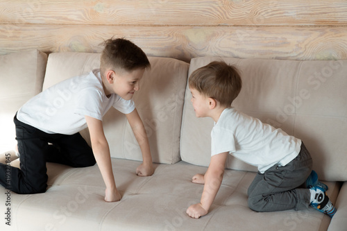 Two boys playing together, sitting on sofa in confrontation position at home, wooden house photo