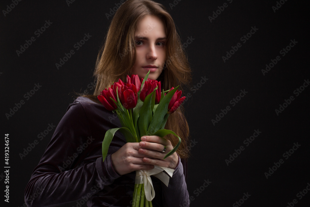 Studio portrait of a young woman on black background with a bouquet of red tulips in her hands Studio portrait of a young woman on black background with a bouquet of red tulips in her hands