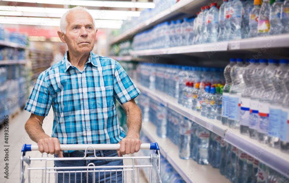 elderly retired man buying bottle of drinking water in alcohol section of supermarket
