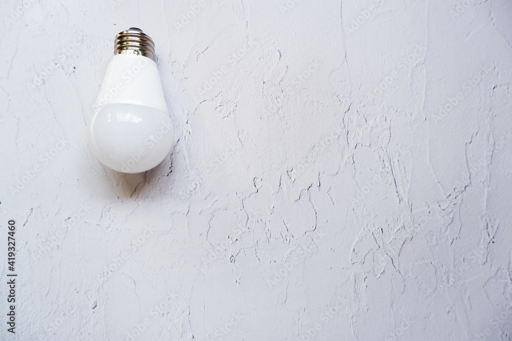 Singular hanging light bulb on vintage white painted background with space for text. 白い塗装壁にぶら下がる電球、LED電球と塗装壁