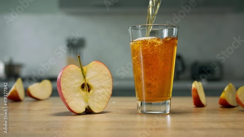 Filling glass with apple juice with apple slices on background. Close up 