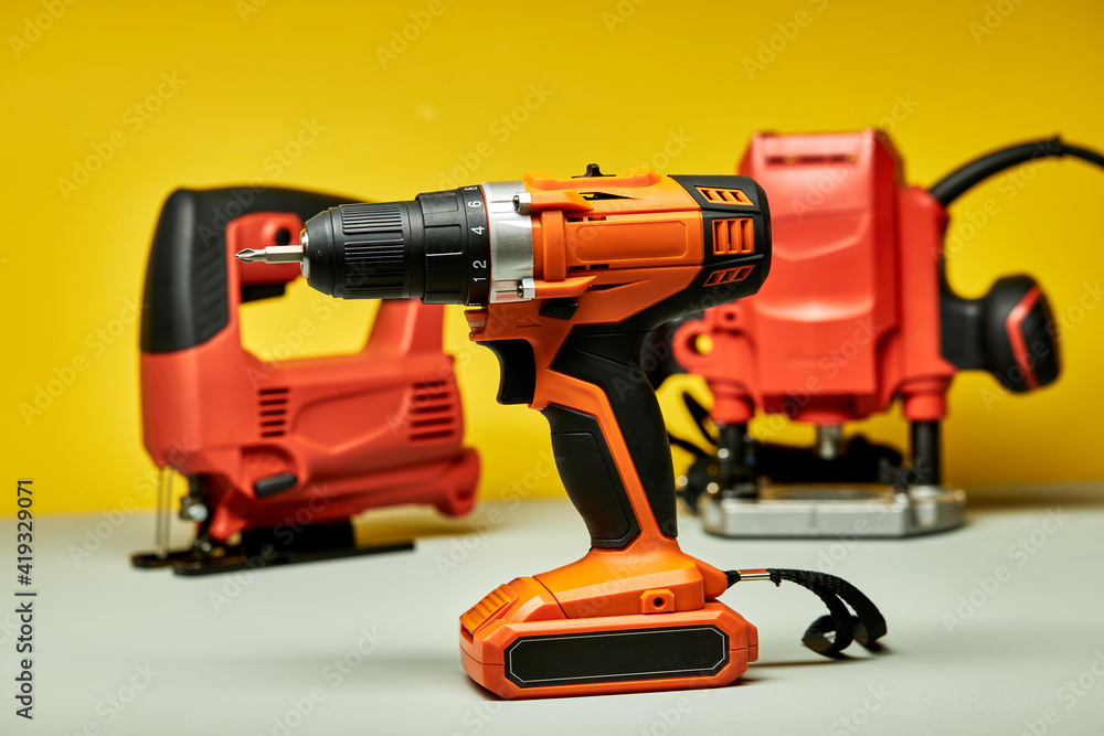 screwdriver, red battery drill with jigsaw in the background, copy space tools instruments