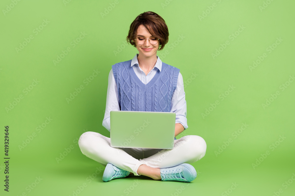 Full length body size photo of girl working on laptop sitting down isolated on bright green color background Full length body size photo of girl working on laptop sitting down isolated on bright green color background