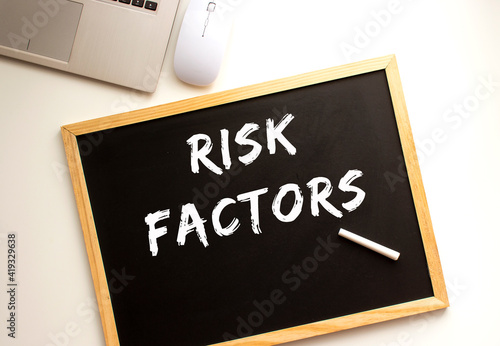 Text RISK FACTORS written in chalk on a slate board. Office desk.