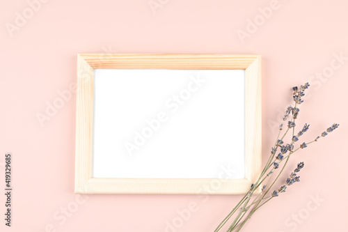 Wooden photo frame with white blank card and lavender flowers on pastel pink background. Mock up poster frame. Stylish template