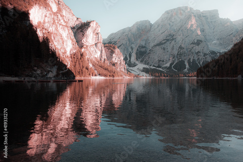 Fantasy colors of the Dolomite mountains in the Braies lake towards sunset with boats moored, South Tyrol, Italy. Concept: relaxation in nature, famous natural places, fantasy colorful scene