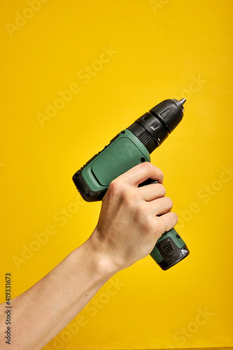 Battery screwdriver or drill in hands isolated over yellow background, cropped male holding tool instrument for repair. copy space