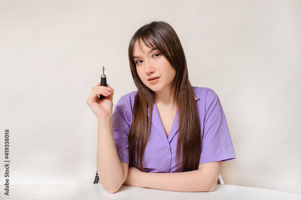 Young woman manicurist is using an electric nail file drill machine on a client's nails. Young woman manicurist is using an electric nail file drill machine on a client's nails.