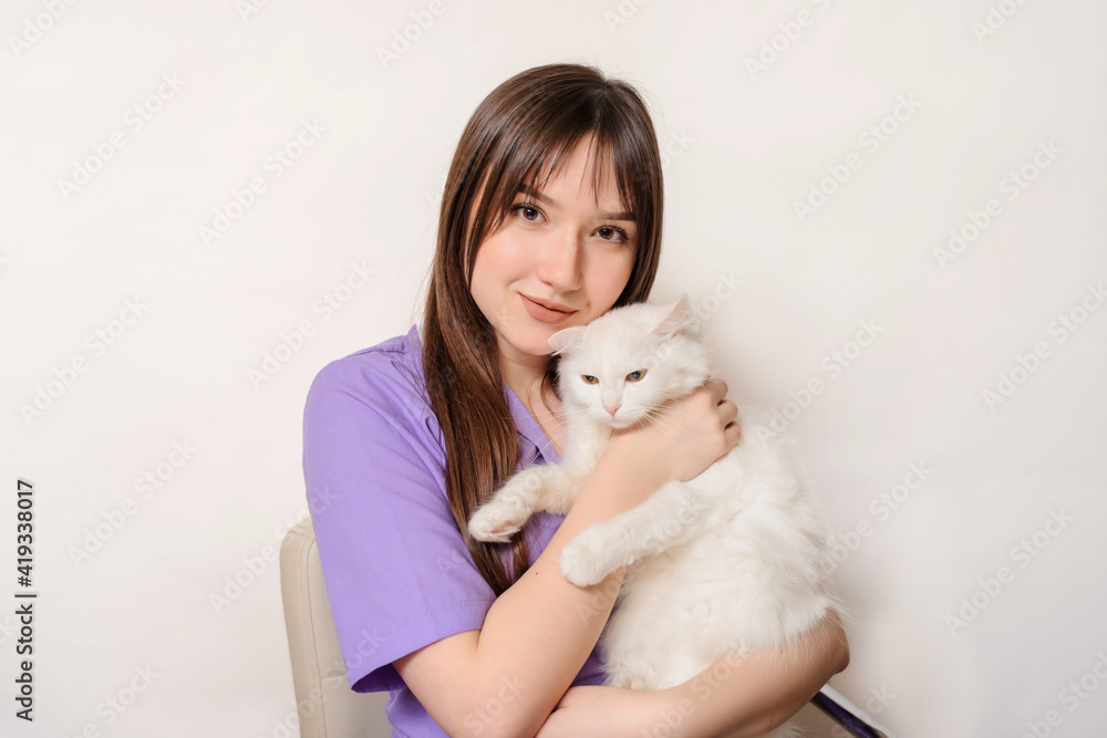 Young woman veterinar in a purple robe is holding a white cat in her hands on white background. Young woman veterinar in a purple robe is holding a white cat in her hands on white background.