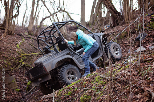 A girl is standing by an SUV that has moved into a ditch. Winch coupled to ATV that drove off after extreme riding