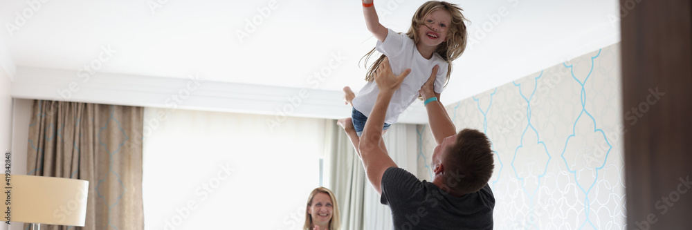 Man tosses laughing child over his head in bedroom. Family relationships and positive atmosphere at home concept Man tosses laughing child over his head in bedroom. Family relationships and positive atmosphere at home concept