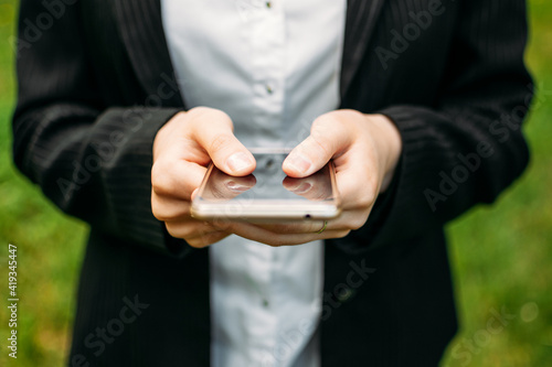 Close up female hands with cell phone on nature background. Smartphone in hand business woman in formal suit
