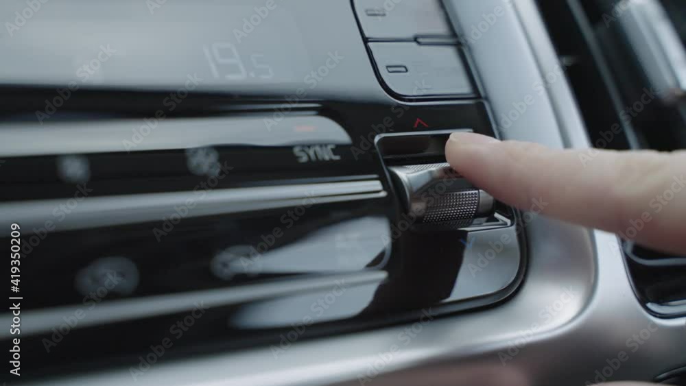 Hand adjusts the air conditioner control buttons in the car. The climate control buttons are silver. The climate system in automatic mode. The Man Regulates The Climate Control In The Car Hand adjusts the air conditioner control buttons in the car. The climate control buttons are silver. The climate system in automatic mode. The Man Regulates The Climate Control In The Car