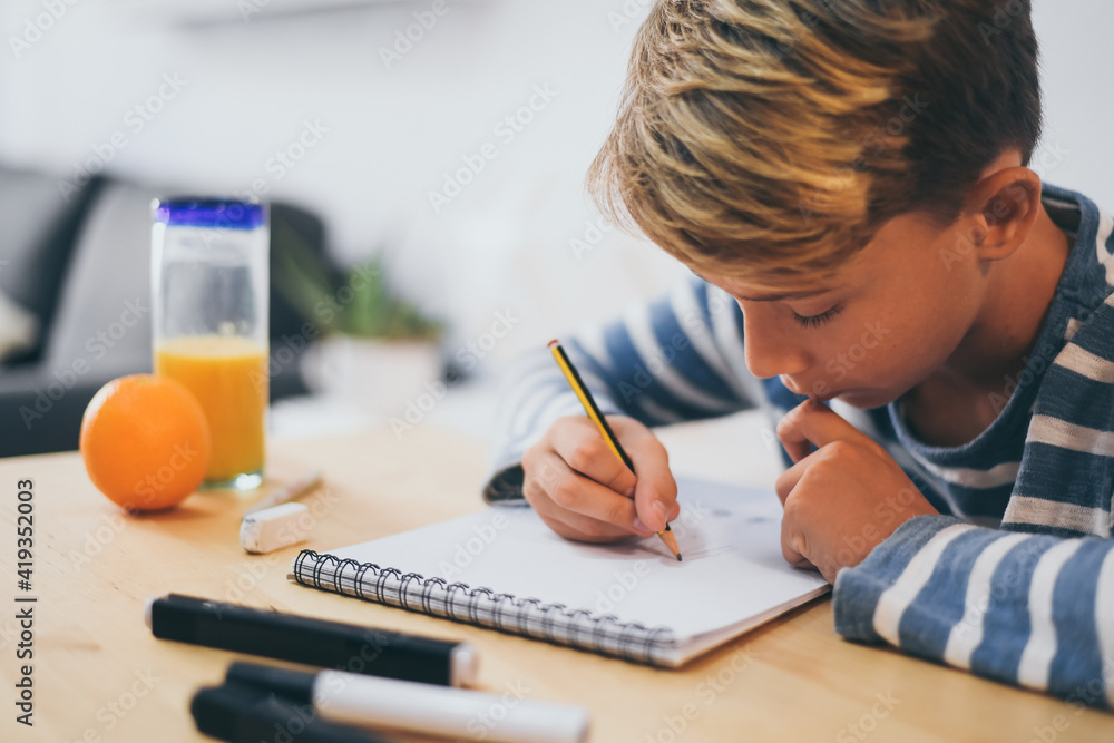 Student drawing with pencil on the notebook. Boy doing homework writing on a paper. Kid hold a pencil and draw a manga at home. Teen drawing sitting at the table. Education art talent ability concept.