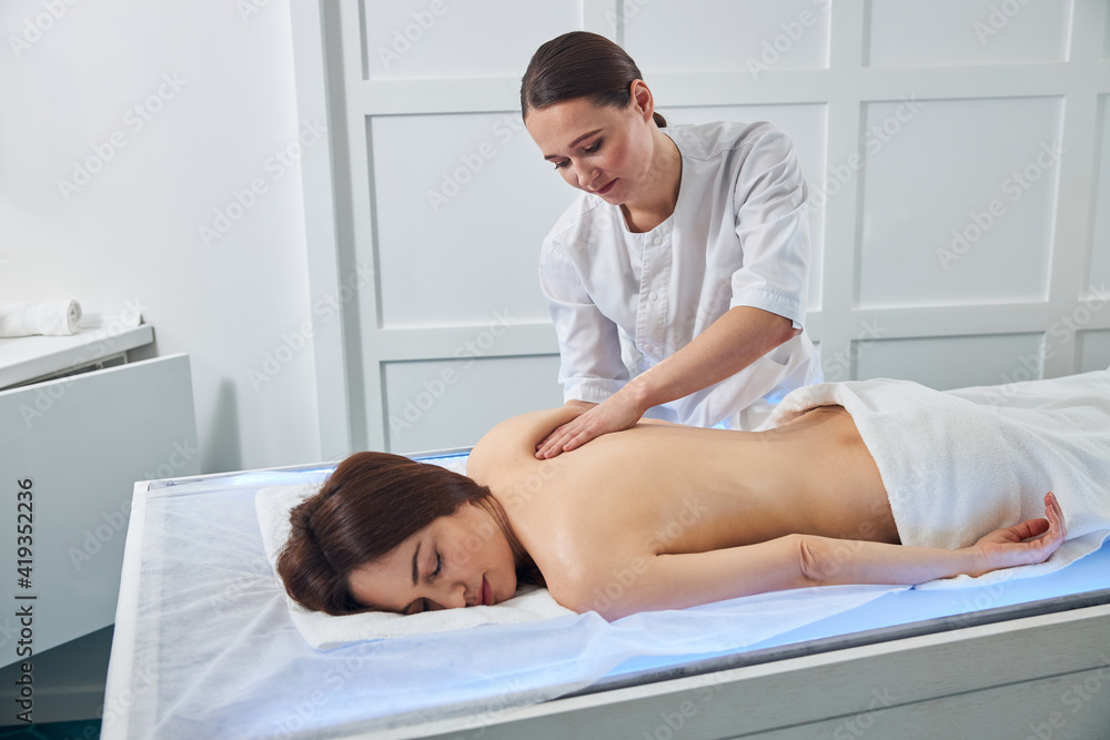 Masseuse kneading the shoulder skin with her palm Masseuse kneading the shoulder skin with her palm