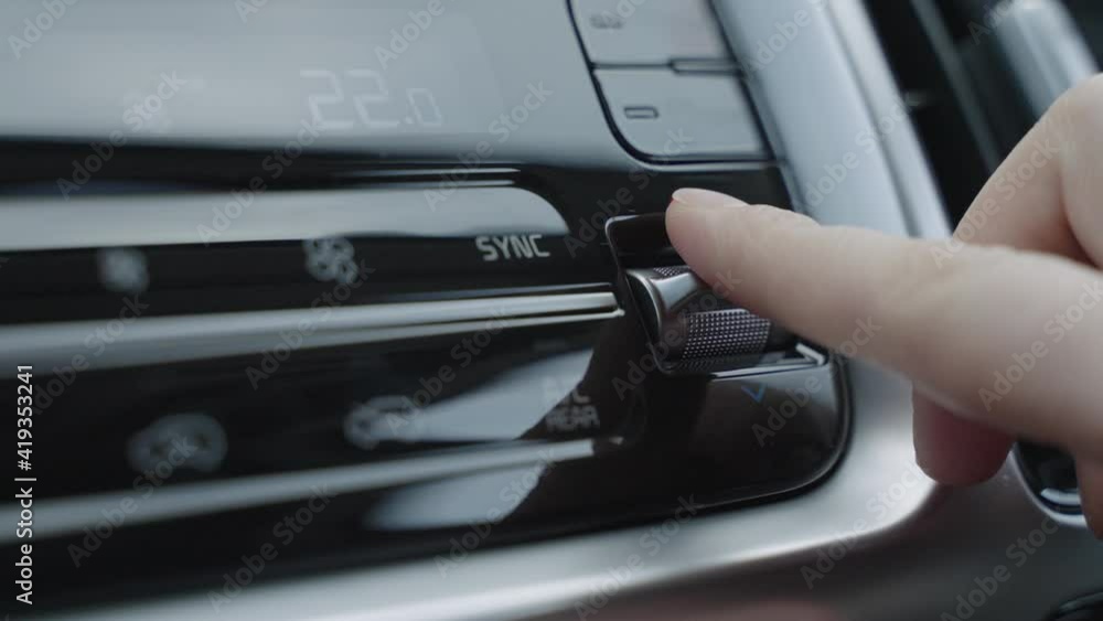 Hand adjusts the air conditioner control buttons in the car. The climate control buttons are silver. The climate system in automatic mode. The Man Regulates The Climate Control In The Car Hand adjusts the air conditioner control buttons in the car. The climate control buttons are silver. The climate system in automatic mode. The Man Regulates The Climate Control In The Car