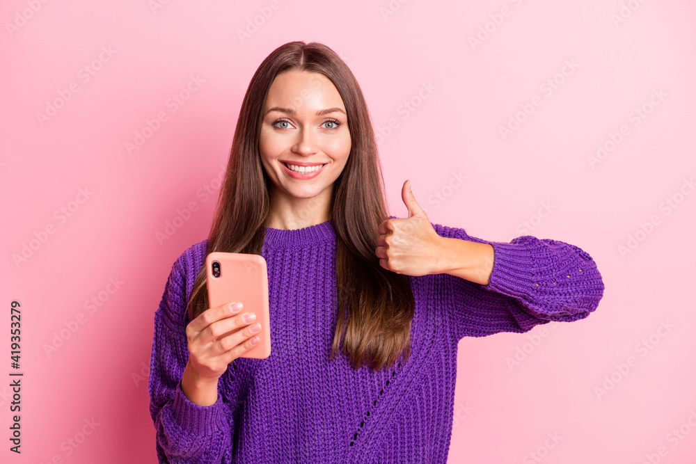 Photo of pretty cheerful lady hold phone show thumb up toothy smile wear sweater isolated on pink color background Photo of pretty cheerful lady hold phone show thumb up toothy smile wear sweater isolated on pink color background