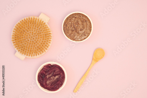 Home body skin care concept. Natural homemade scrub, fruit cream, dry body massage brush and wooden spoon on a pink background. Copy space, flat lay, top view