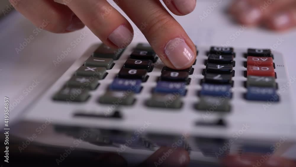 female hand adds the numbers on the calculator and writes down the result female hand adds the numbers on the calculator and writes down the result