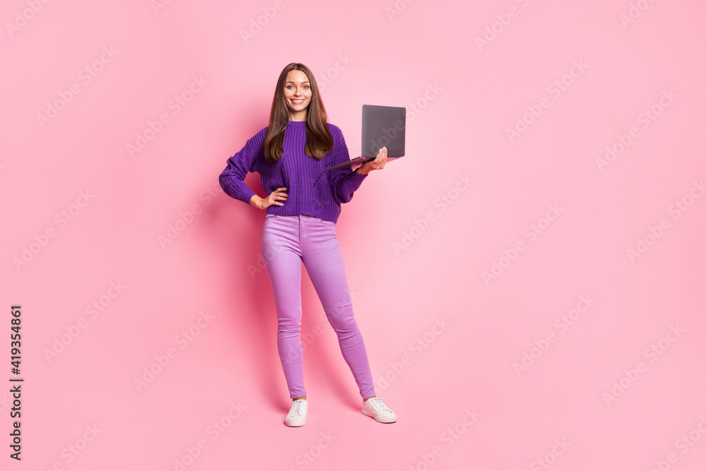 Full size photo of optimistic girl hold laptop wear lilac sweater trousers sneakers isolated on pink background Full size photo of optimistic girl hold laptop wear lilac sweater trousers sneakers isolated on pink background