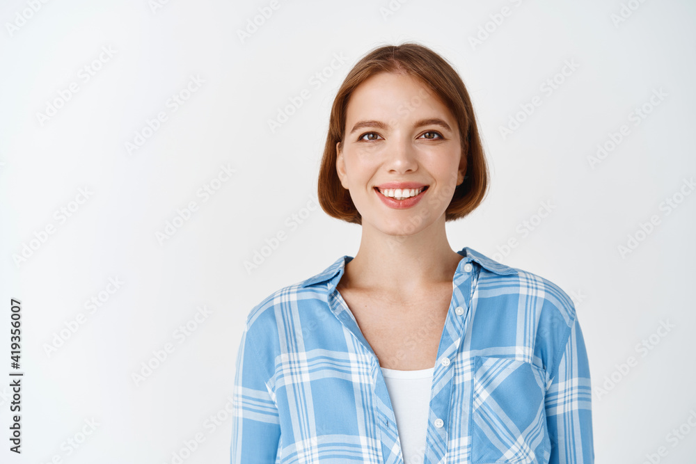 Smiling candid woman in casual clothes looking happy. Young girl with short hair and light make-up standing on white background Smiling candid woman in casual clothes looking happy. Young girl with short hair and light make-up standing on white background