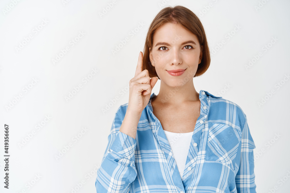 Portrait of smiling confident girl showing way, pointing finger up at top promo, demonstrate advertisement, standing on white background Portrait of smiling confident girl showing way, pointing finger up at top promo, demonstrate advertisement, standing on white background
