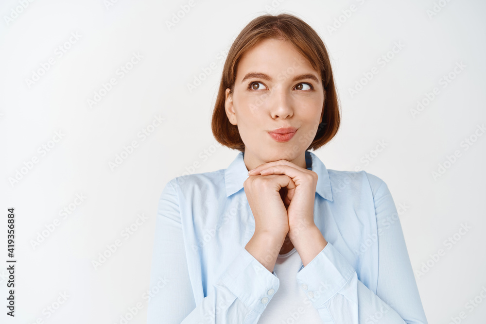 Hmm, let me think. Dreamy and thoughtful girl imaging things, steeple fingers and looking aside with intrigued face, standing in blouse on white background Hmm, let me think. Dreamy and thoughtful girl imaging things, steeple fingers and looking aside with intrigued face, standing in blouse on white background