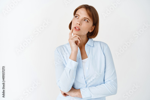 Portrait of young thoughtful woman looking aside at logo, thinking and making choice, pondering decision, standing in blouse against white background