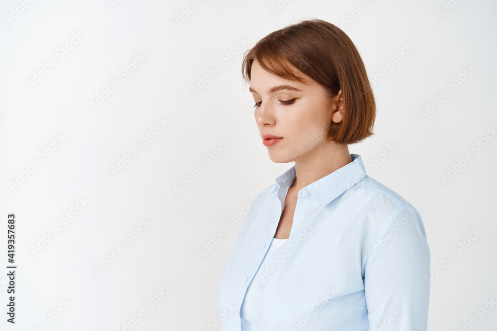 Portrait of young natural girl with short hair, wearing blue blouse, looking down and sideways, standing on white background for your logo Portrait of young natural girl with short hair, wearing blue blouse, looking down and sideways, standing on white background for your logo