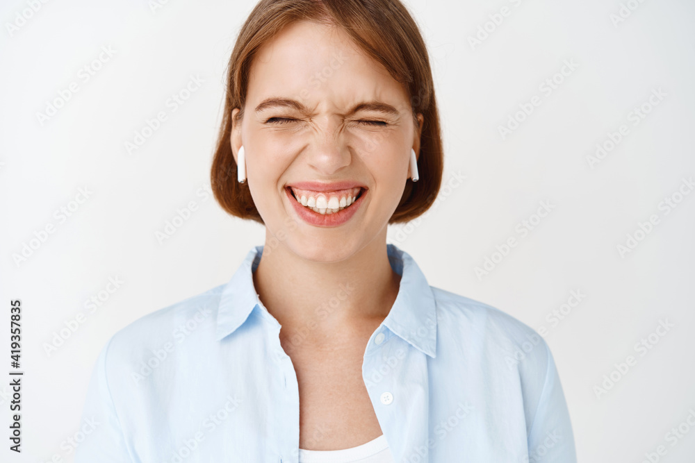 Close-up portrait of excited girl smiling with eyes closed, enjoying listening music in wireless earphones, standing on white background Close-up portrait of excited girl smiling with eyes closed, enjoying listening music in wireless earphones, standing on white background